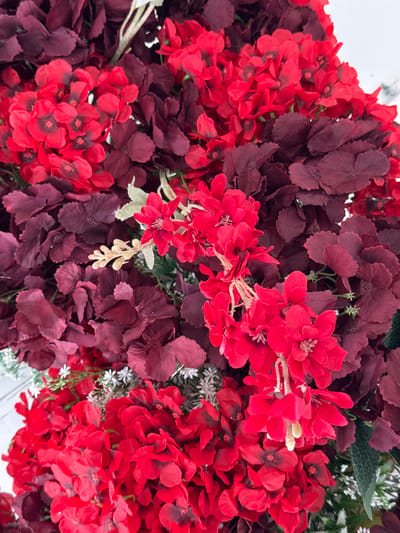 This is a close-up, overhead shot of a floral arrangement featuring numerous clusters of bright red and dark red hydrangea-like flowers, along with some smaller white flowers and green foliage. The flowers are densely packed, creating a rich texture. There are no people or animals present. The arrangement appears to be artificial, likely for decorative purposes. There is no context provided in the image to indicate its location in the city of Tanjungmeru, Indonesia.