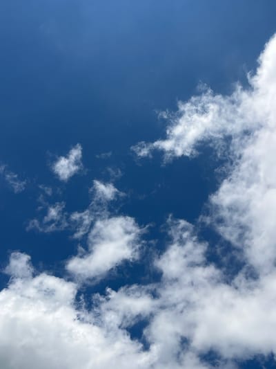 The image displays a clear blue sky with scattered white clouds. The clouds are predominantly cumulus and cirrus formations, appearing fluffy and billowy in some areas and wispy in others. The sky is a deep, vibrant blue, indicative of a bright, sunny day. There are no visible structures, objects, people, or animals in the frame, just the expansive sky and clouds. The location is Psebai, Russia, and the image captures a typical natural outdoor scene.