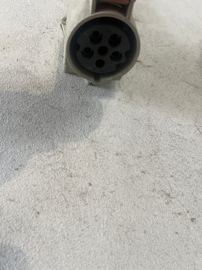 A close-up, high-angle shot shows a light-colored, round electrical connector with five circular openings. The connector is on a textured, light gray surface. The connector is located in the city of Тэльмінскі сельскі Савет, Belarus.