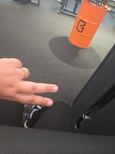 A hand displaying a peace sign with an orange drum and black gym equipment in the background. The location is Zirndorf, Germany.