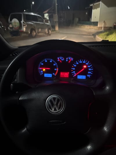 The image shows a view of the dashboard and steering wheel of a Volkswagen car, likely a Golf IV model, at night. The dashboard is illuminated with blue and red lights. The speedometer reads approximately 15 km/h. The odometer displays "271875," and the clock shows "12:53." The temperature is indicated as "8.0°C." A warning light in the lower left of the instrument cluster is illuminated. The steering wheel has the Volkswagen logo in the center. Through the windshield, a dimly lit street and buildings are visible, possibly a residential area or a quiet street at night. The location within Mirkovo, Bulgaria, cannot be determined from the image.