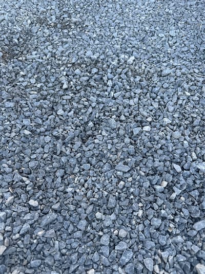 The image shows a close-up, overhead view of a gravel surface. The gravel is composed of small, angular, grey stones of varying sizes, densely packed together. There are no people, animals, or discernible structures visible in the frame. The lighting suggests an outdoor setting, possibly during the daytime, with shadows cast by the stones indicating a light source from above. The texture of the gravel is rough and uneven. There is no information in the image to determine the specific location in Izyayu, Russia.