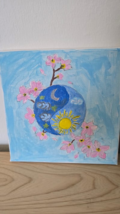 The image is a painting on canvas depicting a yin-yang symbol surrounded by cherry blossoms. The background is a light blue color. The yin-yang symbol is divided into two halves: one side features a yellow sun and the other a silver crescent moon. The cherry blossoms are painted in shades of pink and white. The painting is hanging on a wall, with a white wall on the left and a wood-paneled wall on the right. There are no people visible in the image. The location in Zirndorf, Germany is not discernible from the image.