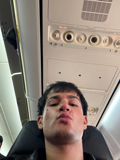 The image is taken inside an airplane cabin, likely during a flight or while stationary. The primary subject is a person with dark hair, lying back in their seat. The cabin interior is visible, showing overhead panels with air vents and storage compartments. There are no indications to determine the location as Casorate Sempione, Italy.