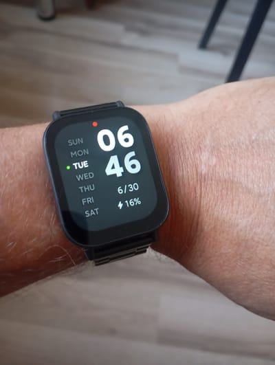 A close-up shot focuses on a smartwatch worn on a person's wrist. The watch face displays the time as 06:46, the date as 6/30, and a battery level of 16%. Below the time, the days of the week are listed, with "TUE" highlighted by a green dot, indicating it is Tuesday. The background consists of a wooden floor, suggesting an indoor setting. The image does not provide any information about the location in the city of Ararat, Armenia.