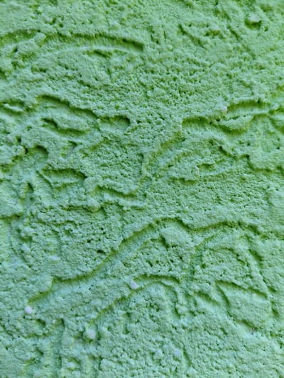 The image is a close-up, abstract view of a textured, lime-green surface. The surface has a rough, porous quality with visible ridges and undulations. There are no discernible people, objects, or actions. The environment is undefined beyond the immediate texture of the surface. There is no identifiable location within Petreni, Moldova.