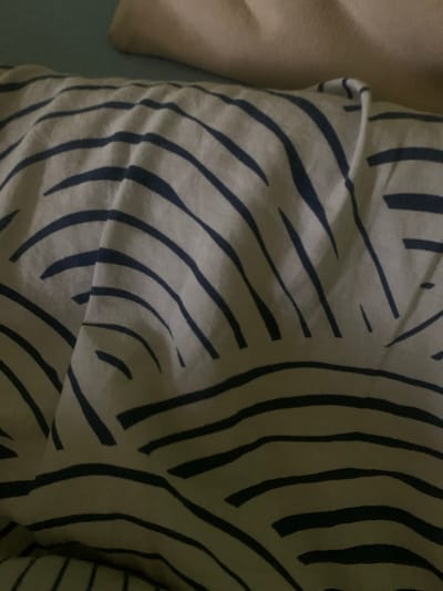 The image shows a close-up of a striped blanket or bedspread with navy blue stripes on a light background. The fabric is wrinkled and folded, indicating it is likely in use. In the upper part of the image, a light-colored surface, possibly a pillow or a part of a bed, is visible. The lighting is dim, casting shadows on the fabric. The image does not contain any information that would allow for its location to be determined in Skarydzew, Poland, or any other specific geographical location. There are no people, actions, or interactions depicted.