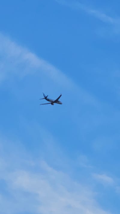 The image shows a passenger airplane in the sky. The airplane is viewed from below, and it appears to be in the process of banking or turning. The sky is a clear blue, with some scattered white clouds. The lighting suggests it is daytime, possibly mid-morning or afternoon. The image is taken from the ground, looking upwards. There are no people visible, only the airplane as the primary object. The setting is an open sky, indicative of a flight path over an outdoor area. The scene is peaceful and ordinary, depicting a common occurrence of air travel. There is no visible text in the image. The location context provided is Панфилово, Kazakhstan, which implies the airplane is flying over this region.