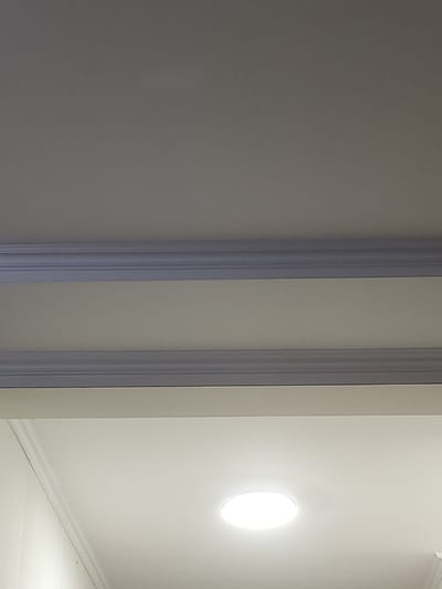 The image shows a close-up view of a ceiling with decorative molding. There are two horizontal bands of molding, with a lighter colored section of the ceiling between them and above them. A circular light fixture is visible on the lower part of the ceiling. The setting appears to be indoors. There is no visible indication of the city of Жарлыкөл, Kazakhstan.
