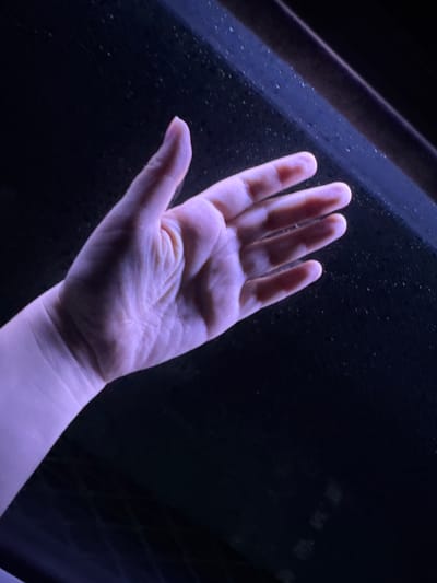 A human hand with visible veins and skin texture is held open, palm facing upwards. The hand is illuminated by a purple light. The background is dark and appears to be a surface with small, scattered white specks. The upper right portion of the image shows a diagonal dark line, possibly a ledge or the edge of an object. The image does not provide any identifiable elements related to the city of Ninh Tây, Vietnam.