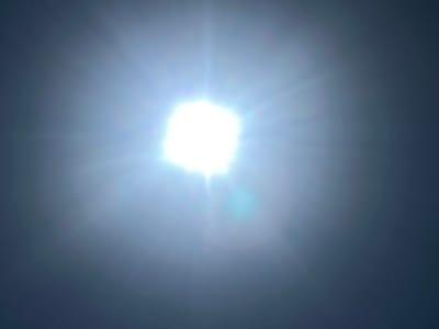 The image displays a bright, sun-like object at the center, emitting rays of light in all directions. The background transitions from a light, hazy blue around the central object to a dark blue or gray towards the edges. The overall impression is of the sun viewed through a hazy atmosphere, possibly with lens flare. There are no discernible human figures, animals, or man-made structures in the image. The scene appears to be an outdoor environment, likely the sky, with no specific urban or natural landmarks visible. The location in Sheregesh, Russia, cannot be determined from the visual information presented in the image.