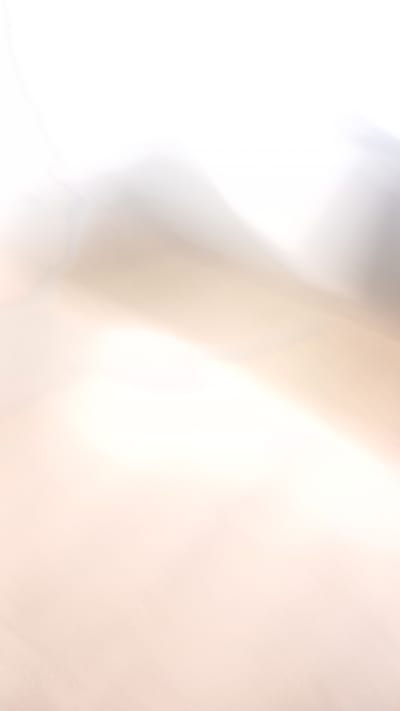 The image is an abstract, out-of-focus shot of what appears to be a landscape with soft, blended colors. Dominant tones are white, light gray, and a pale peachy-beige, creating a dreamy and ethereal effect. The background is a bright, almost blown-out white, suggesting strong lighting or an overexposed setting. Subtle shadows and highlights suggest contours or shapes, possibly hills or dunes, without distinct features. The texture appears slightly grainy, consistent with digital photography. The overall impression is of a serene, perhaps natural, environment rendered in a highly impressionistic manner. The image does not provide any recognizable landmarks or specific details that would allow for identification of a precise location within Oliveira do Bairro, Portugal.