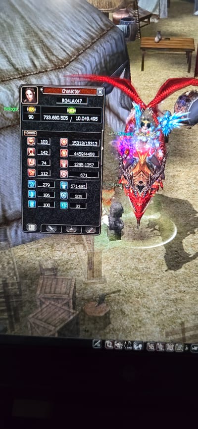 The image shows a screenshot from a video game, likely an MMORPG. The primary focus is a character's inventory and status screen on the left, with the in-game environment visible on the right.
**Character Information:**
* The character's name is "RG4LAK47".
* The character's level is 90.
* The character's experience points are 733,680,505 out of 10,049,495.
* The character is identified as a "Biologist".
* Various stats are displayed in columns, including numerical values such as 103, 142, 74, 112, 279, 186, 100, 15313/15313, 4459/4459, 1285-1357, 671, 671-681, 505, and 33.
**In-Game Environment:**
* The character is in what appears to be an outdoor area with a rough, dirt or grassy ground texture.
* There are wooden crates and a small wooden table with what looks like pottery on it in the background.
* A tent-like structure is visible behind the character's information panel.
* The character on the right is equipped with elaborate red and blue winged armor and a horned helmet. The character is on some sort of mount or creature.
**Location:**
There is no information within the image that indicates the location is the city of Villing, France. The visual elements are consistent with a fantasy video game setting.