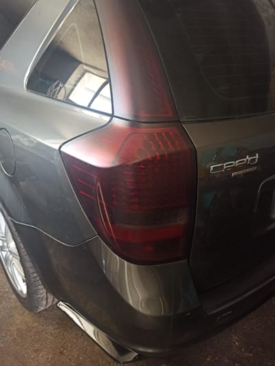 The image shows the rear of a dark gray vehicle, a Dodge Caliber Navigator, parked indoors. The taillight is a dark red color. The vehicle is partially in view. A tire is visible in the bottom right corner. The location is Krushare, Bulgaria is not determinable from the image.