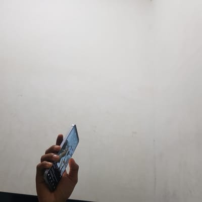 A hand holds a smartphone against a light grey background. The smartphone screen displays an image. The location is indiscernible.