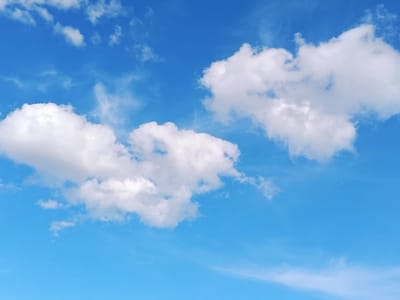 The media file is a photograph of a bright blue sky with scattered white clouds. The clouds vary in size and density, with some appearing wispy and thin, and others more substantial and puffy. The lighting suggests it is daytime, likely mid-morning to early afternoon, with the sun illuminating the clouds from above, creating bright white highlights and some shadowed undersides. The overall impression is one of a clear, pleasant day. There are no people or objects visible in the frame, and no text is present. The setting is an open sky, typical of an outdoor scene. The weather appears to be fair and sunny. Based on the provided location context, this scene is likely taking place in Lahojsk selsoviet, Belarus. The image evokes a sense of calm and openness.