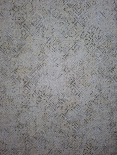 This is a full-frame, eye-level, medium shot of a textured surface with a geometric pattern. The pattern consists of interlocking diamonds and squares rendered in muted tones of beige, cream, and gray. The texture appears to be that of fabric or wallpaper, with a slightly rough, woven appearance. The lighting is even, suggesting it is indoors or under overcast conditions, with no distinct shadows to indicate a specific time of day. There are no people, objects, or any discernible scene or setting visible in the image. The activity, if any, is not apparent. No text is present in the image. The provided location context is Keles, Uzbekistan, but there are no visual cues within the image itself to suggest this location.