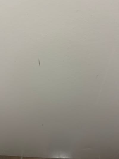 The image shows a plain white wall with a few small, light-colored marks on the surface. There are no people, objects, or actions in the image. The coordinates provided are for the city of Lyon, France, not Les Belleville. There is no information to indicate this is a scene in Les Belleville.