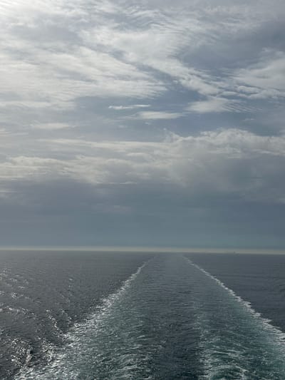 The image shows a seascape under a cloudy sky, likely taken from a moving vessel. The right side of the image features dark, choppy water with a distinct wake created by the vessel. The left side shows a sky filled with various cloud formations, ranging from wispy cirrus clouds to denser, more uniform cloud layers. There are no visible people or other objects in the image. The overall scene is characterized by the contrast between the turbulent water and the textured sky. The location is unknown, and there is no evidence indicating it is in Unknown, France.