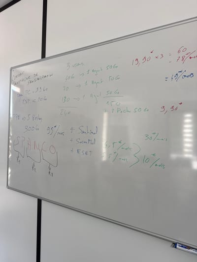 The image shows a whiteboard with handwritten notes and calculations, likely in an office or meeting room. The whiteboard is positioned against a plain white wall, with a black vertical frame visible on the left side. The lighting suggests an indoor environment.
The content on the whiteboard appears to be related to a project or business plan, with sections labeled "COMBAT CAMPAGNE DE SENSIBILISATION," "TPE => 5 Postes," and the word "SPANCO" broken down into letters with associated annotations "R1," "R2," and "R3." There are also various numerical calculations, including sums, multiplications, and cost estimations in Euros, indicated by "€" and "mois" (months). Some calculations involve figures like "3 users," "40 Go," "70," "130," "150," and prices such as "59,60," "20,60," "95€/mois," "4,5€/mois," "5,5€/mois," and "30€/mois." There are also red markings for a calculation: "19,90€ x 3 = 60 - 78€/mois" and "= 49€/mois."
The location is identified as Les Arcs, France, which is a well-known ski resort in the Savoie department of the French Alps. The overall scene suggests a professional setting where strategic planning or financial projections are being discussed.