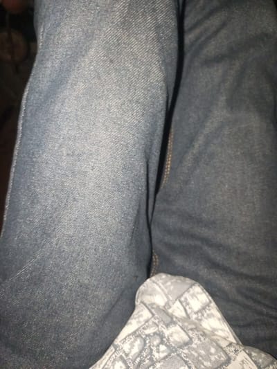 The image shows a close-up view of a person's legs wearing blue jeans. The fabric of the jeans is textured and appears to be denim. There is a small section of patterned fabric visible at the bottom of the image, which is light-colored with a darker, possibly snake-like pattern. The lighting suggests an indoor setting, possibly at night. The location in Agbara, Nigeria, is not visually evident from the provided image.