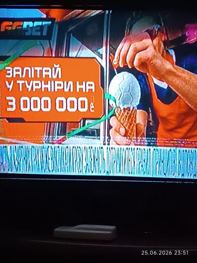 The image shows a television screen displaying a promotional advertisement. The advertisement features text in Cyrillic, including "ЗАЛІТАЙ У ТУРНІРИ НА 3 000 000 €", which translates to "Fly into tournaments for 3,000,000 €". There is also a logo at the top left that appears to say "GABET". In the center right of the screen, a person's hands are visible, holding what looks like an ice cream cone topped with a miniature soccer ball. The background of the advertisement is orange with some graphic elements. Below the advertisement, there is a visual distortion that resembles a striped pattern. The bottom of the image shows the dark casing of a television set and a date stamp that reads "25.06.2026 23:51".

There is no information in the image that indicates a specific location in the city of Bolhrad, Ukraine. The image is a photograph of a television screen, likely taken indoors.