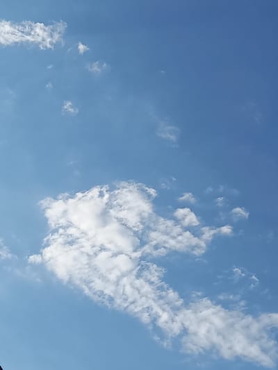 The image shows a clear blue sky with scattered white clouds. The clouds vary in size and density, with some appearing wispy and others more substantial. The lighting suggests it is daytime, with the sun likely high in the sky. There are no discernible landmarks or structures visible, making it impossible to determine a specific location within Keles, Uzbekistan. The scene is a natural, open-air environment, focusing solely on the atmospheric conditions.