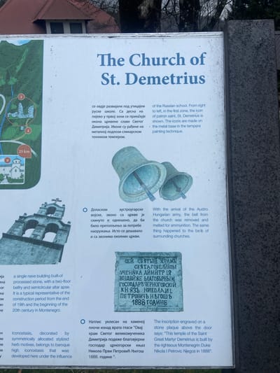 The image is a signpost for the Church of St. Demetrius in Kolašin, Montenegro. The sign is mounted on a dark gray stone base. It provides information about the church in both Serbian and English, including details about its history, architecture, and artistic elements. A map shows the location of the church. The sign includes images of the church's bells and an inscription plaque on the building. The information on the sign covers topics such as the influence of the Russian school, the removal of bells by the Austro-Hungarian army, and the inscription about the building's construction by Duke Nikola I Petrovic Njegos in 1888.