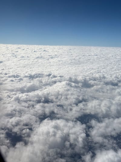 A bright blue sky meets a thick layer of white and gray clouds, creating a distinct horizontal division in the image. The cloud cover appears dense and textured, with shadows adding depth. The blue section is clear and uniform, providing a stark contrast. The perspective suggests a high vantage point, possibly from above the cloud layer. The photograph has a slightly tilted angle.