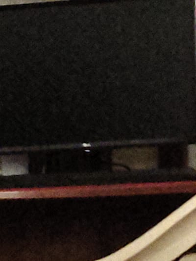 The image shows a close-up of a dark, textured surface, likely fabric or a rough material, on the left side. To the right of this dark surface, there is a vertical red-colored element, possibly a strip of plastic or painted metal. Further to the right, a portion of a light-colored, curved object is visible, which appears to be made of a smooth, possibly glossy material. The overall impression is of an abstract composition focusing on textures and colors, with no discernible human figures, specific objects of recognizable function, or clear environmental cues. The lighting is dim, and the image quality is grainy, making it difficult to discern finer details. There is no visible text in the image. The location context provided, Melitopol, Ukraine, does not offer any visual clues within the image itself.