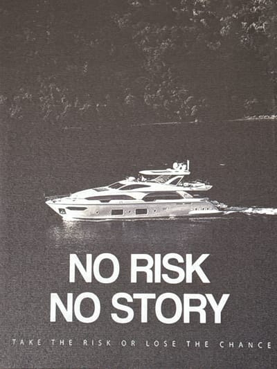 The image is a photograph of a yacht sailing on the water. The yacht is white and sleek, with multiple levels and windows. The water appears calm, with a light wake behind the yacht. In the background, there is a dark, textured area that could be foliage or a hillside. Below the yacht, large white text reads "NO RISK NO STORY". Below this, smaller white text says "TAKE THE RISK OR LOSE THE CHANCE". There are no people visible in the image. The image is a close-up shot, with the yacht occupying the central portion of the frame. The overall tone of the image is monochromatic, with a dark background and white text and yacht.