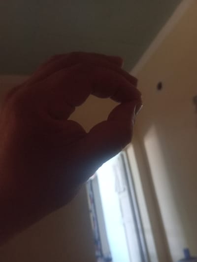 A person's hand is silhouetted against a softly lit background, forming an "okay" gesture. The thumb and index finger are touching to create a circle, while the other fingers are extended. The background appears to be an interior space with a wall and possibly a doorway. The lighting suggests it is likely indoors, with some ambient light illuminating the scene. The exact location in Kyzyltepa, Uzbekistan, is not discernible from the visual information present in the image.