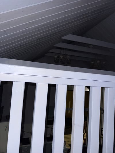 The image captures an interior view looking upwards towards a sloped, white-paneled ceiling. In the foreground, a white railing with vertical balusters is visible. Beyond the railing, several light fixtures with glass shades are suspended from the ceiling. The overall impression is of a modern interior space, possibly a room or hallway with a vaulted ceiling. The location in Doma 1096 Km, Russia, is noted, but there are no specific visual cues in the image to confirm this exact geographical placement or to identify any people, actions, or interactions.