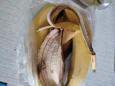 This media file shows a close-up view of a banana peel and one banana inside a clear plastic bag. The setting appears to be indoors, possibly on a table with a light-colored, textured surface. The background is out of focus but suggests a domestic or kitchen environment. The lighting is neutral, and there are no clear indicators of the time of day or weather. The overall scene is simple and focused on the fruit and its peel. There is no text visible in the image. The location context provided is Денисово, Russia.