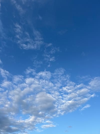 The image shows a bright blue sky with scattered white clouds over the city of Мартемьяново, Russia. The clouds are varied, with some appearing wispy and high in the atmosphere, while others are more dense and billowy lower down. There are no people, subjects, objects, or actions visible in the image, only the natural environment of the sky. The lighting suggests it is daytime.