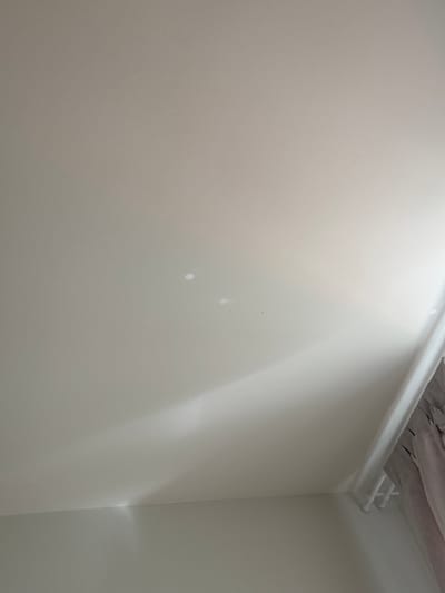 The image shows a corner of a room. The walls are painted in a light neutral color. A white pipe runs along the ceiling, near the corner. The ceiling above the pipe appears to be unfinished with visible material. There are some minor imperfections on the wall. No people are visible. The location cannot be confirmed as Люк, Russia, from the visual information provided.