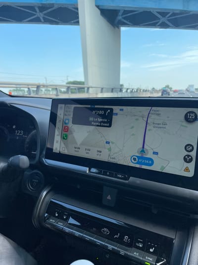 A car's infotainment system displays a navigation app with a route indicating a distance of 34.6 kilometers. The destination is La Spezia, 80 kilometers away via the A15 highway towards Parma Ovest. The car is driving at 125 kilometers per hour. The climate control panel shows a temperature setting of 18.5 degrees Celsius, and the air conditioning is on. The gear shift is visible, along with the power button and speedometer reading 123.