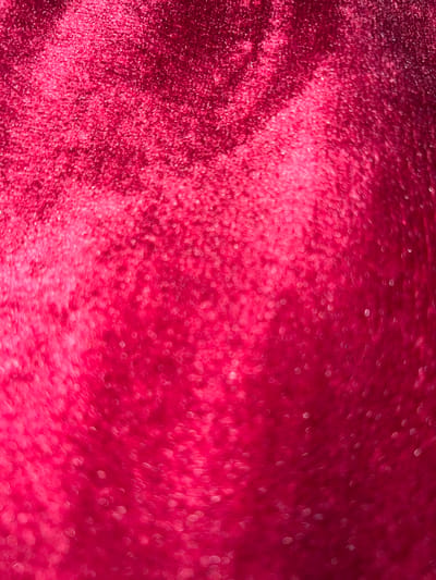 The image is an abstract close-up of a textured surface, appearing to be a deep red velvet or plush fabric with a glittery or sparkling effect. The lighting creates a bokeh effect, with circular blurs of light scattered across the surface, particularly concentrated in the lower half and to the right. The texture of the fabric is visible, with a soft, velvety nap. There are no discernible objects, people, or environmental features to indicate a specific location within Schoonderbuken, Belgium. The image is purely a visual study of texture, light, and color.