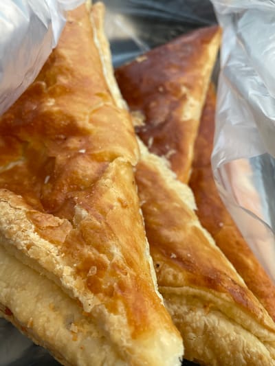 The image shows a close-up view of several triangular pastries inside a clear plastic bag. The pastries have a golden-brown, flaky crust. The environment appears to be indoors, though specific details about Khoronk, Armenia are not discernable from the image.