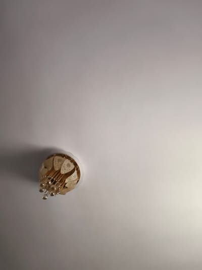 A chandelier hangs from a white ceiling. The chandelier is gold with crystal droplets. The location is not discernible.