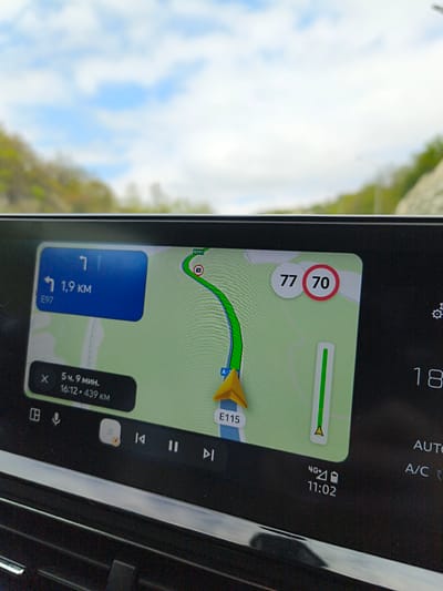 The image shows a car's infotainment system displaying a navigation app. The map indicates the vehicle is on the E115 highway. The navigation suggests turning left in 1.9 km onto E97. The current speed is 77, while the speed limit is 70. The ETA is 5 hours and 9 minutes with a remaining distance of 439 km, arriving at 16:12. The time is 11:02 with a 4G+ connection. The infotainment system also shows the temperature is 18, and the AC is on auto.
Given the presence of the E115 highway marker, it's highly probable the location is somewhere in Russia, as the E115 route passes through it. However, based solely on this image, it's not possible to confirm the exact location. While "Verkhnebakanskiy, Russia" might be possible given its proximity to the E115, there is no direct confirmation of that in this image.