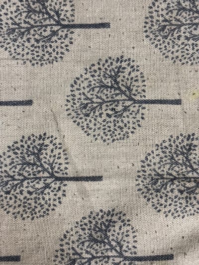 The image shows a close-up of a fabric with a repeating pattern of stylized trees. The trees are dark gray and appear to be printed on a light beige, textured background that resembles linen or burlap. Each tree has a dark trunk and branches, with a dense, dotted canopy suggesting leaves. The trees are oriented in various directions, with some cut off by the edges of the frame, indicating a larger repeating pattern. The fabric is a textile material and there are no people, objects, actions, or interactions depicted in the scene. The location in Svkh Maslovskiy 1 Otdeleniye, Russia, is not evident from the visual information in the image.