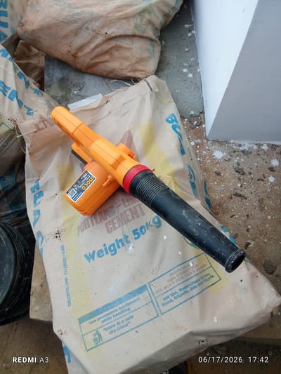 The image shows an orange and black leaf blower lying on top of two large bags of Portland cement. The cement bags are light brown and have blue lettering. One bag has "PORTLAND CEMENT" and "Weight 50kg" printed on it. The other bag has the beginning of blue lettering visible. The leaf blower has the brand "INGCO" on its side, along with some model information and a QR code. The scene appears to be outdoors, with loose dirt, small white specks of paint or plaster, and some debris on the ground. To the right, a white, angled structure, possibly a wall or pillar, is visible. In the lower left corner, the text "REDMI A3" is present, and in the lower right corner, the date and time "06/17/2026 17:42" are displayed. The location is identified as Nawfia, Nigeria, as indicated by the address on the cement bag: "KM 184, Benin-Okpella Express, Road, Okpella, Edo State, Nigeria," which is in the vicinity of Nawfia.