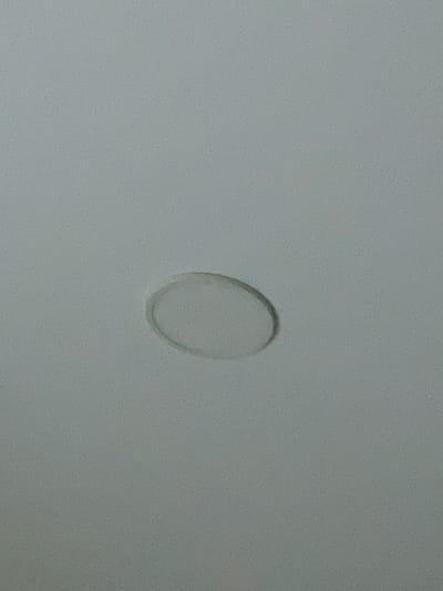 This media file is a close-up, high-angle shot of a faint, translucent oval shape on a textured, matte, light gray surface. The oval appears to be a subtle indentation or discoloration, with a slightly darker edge and a lighter center. The surface itself has a granular texture, suggesting it could be a wall, a piece of furniture, or some other solid material. There are no people, animals, or other discernible objects in the frame, nor is there any indication of a specific setting, time of day, or weather conditions. The overall impression is one of simplicity and minimalism, focusing solely on the texture and the subtle anomaly within the surface. There is no visible text in the image. The location context provided is Sumqayit, Azerbaijan, but this information is not visually evident from the image itself.