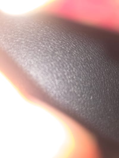 The image shows a close-up, out-of-focus view of a textured black surface, possibly leather or similar material. A blurry pink or red area is visible on the left side of the frame. The right and bottom sections are overexposed, appearing as bright white with orange and yellow light flares. The location in the city of Pintomakmur, Indonesia is irrelevant because the image does not depict any geographical landmarks or specific features indicative of that location.