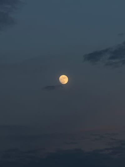 The image shows the moon in a dark, cloudy sky. The moon is nearly full and appears to be slightly yellow. Clouds are scattered across the sky, some darker than others. It is unlikely to identify the location in Civitavecchia, Italy, without further visual reference or geo-specific information.