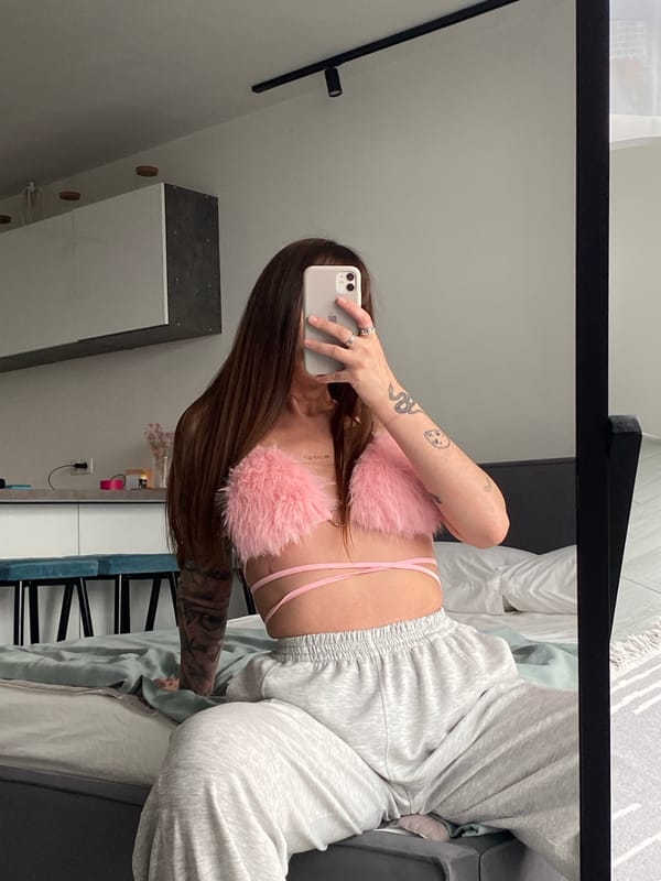Mirror selfie in a bedroom, pink fuzzy top and grey sweatpants