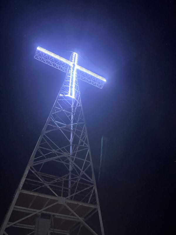 Blue-lit cross glows atop steel structure in nighttime observation