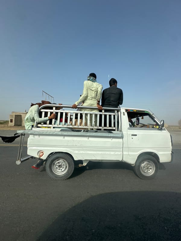 White pickup truck carrying passengers along a Pakistani road