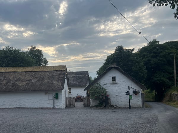 Thatched cottages and rolling hills on a cloudy evening.